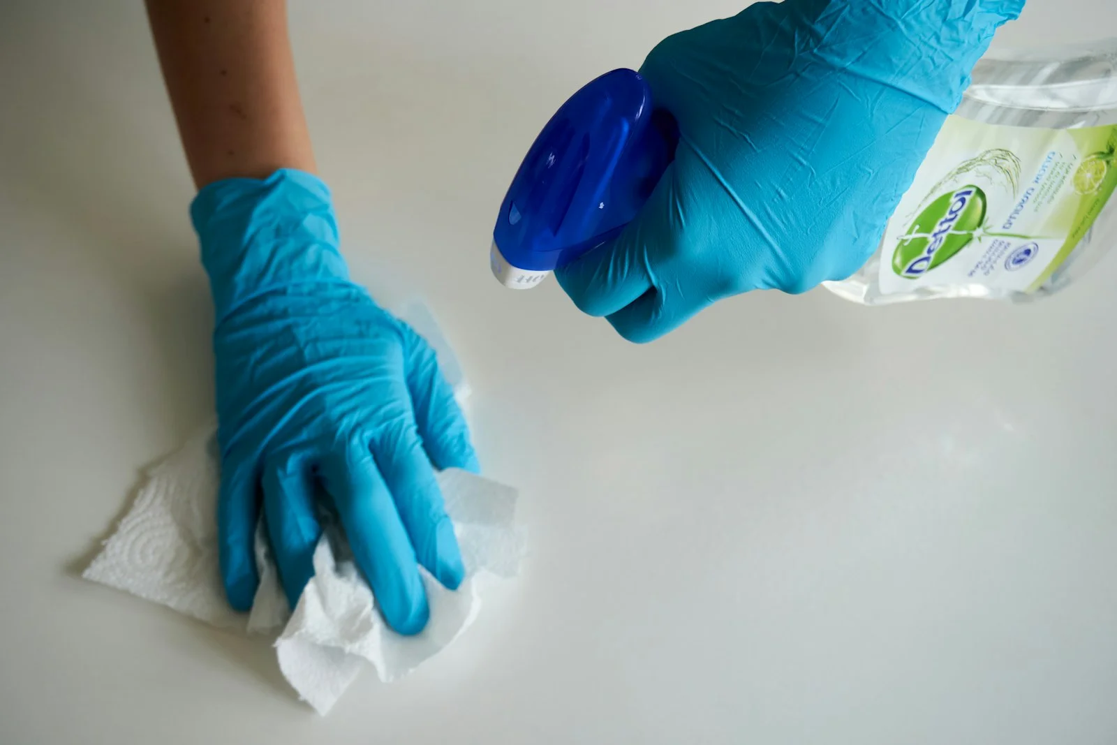 Gloved hands holding Dettol spray and wiping a white surface with paper towel during deep cleaning