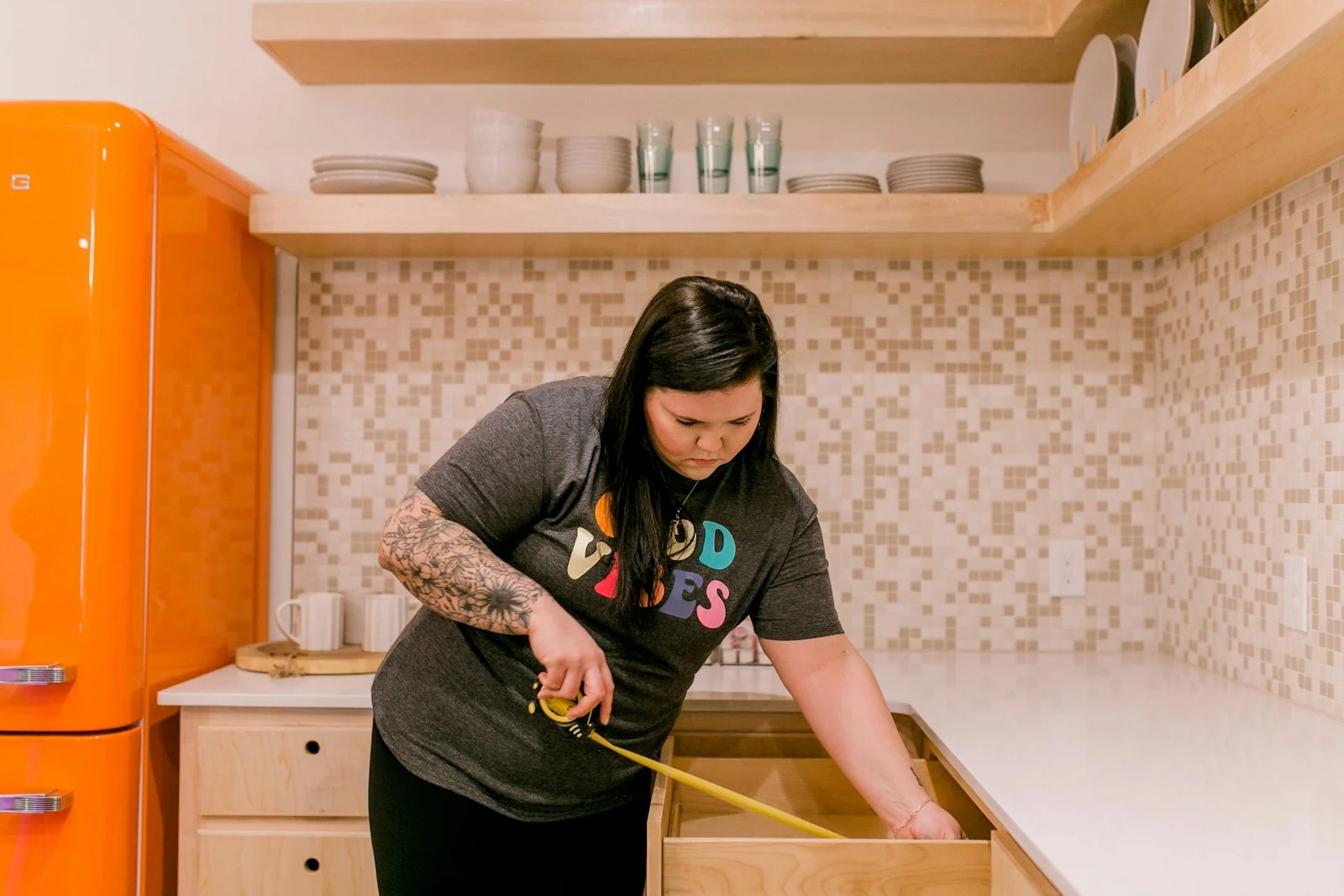 A woman measures a kitchen drawer with a tape measure